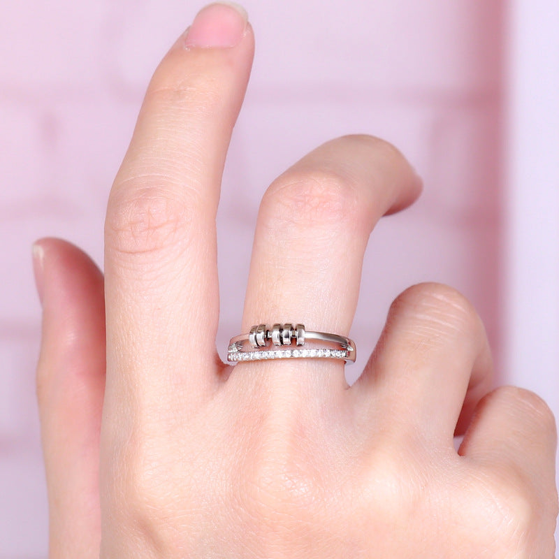 Anillo Axia: Anillo moderno con patillas paralelas y detalles cilíndricos de metal pulido.