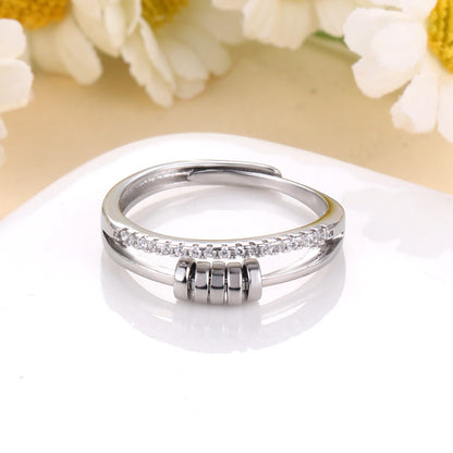 Anillo Axia: Anillo moderno con patillas paralelas y detalles cilíndricos de metal pulido.